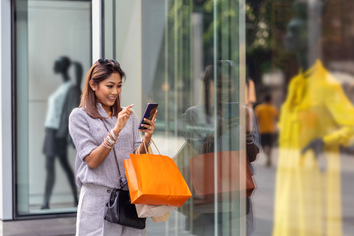 Asian woman using the smart mobile phone for check online shopping order is completed with clothes beside the glassess in store shop with happy action at department center