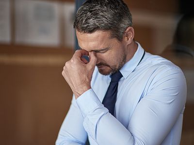 stressed businessman with his head down and fingers pinching his nasal bridge