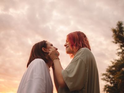 Happy young woman touching her girlfriends cheeks at sunset