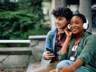 Happy looking college couple listening music together while relaxing at campus. 