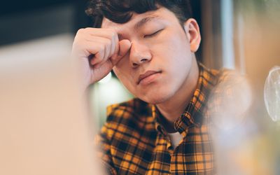 man sitting at his desk looking tired rubbing his eyes