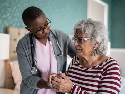 Black nurse helping elderly white woman in her bedroom