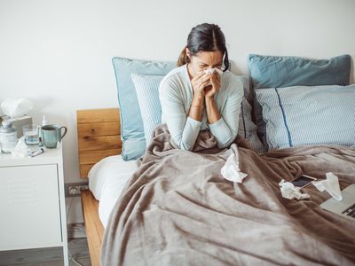 Woman with a cold blowing her nose in bed