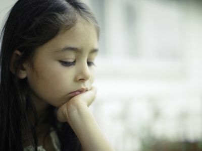 Eight year old girl sits beside window on rainy day in contemplation