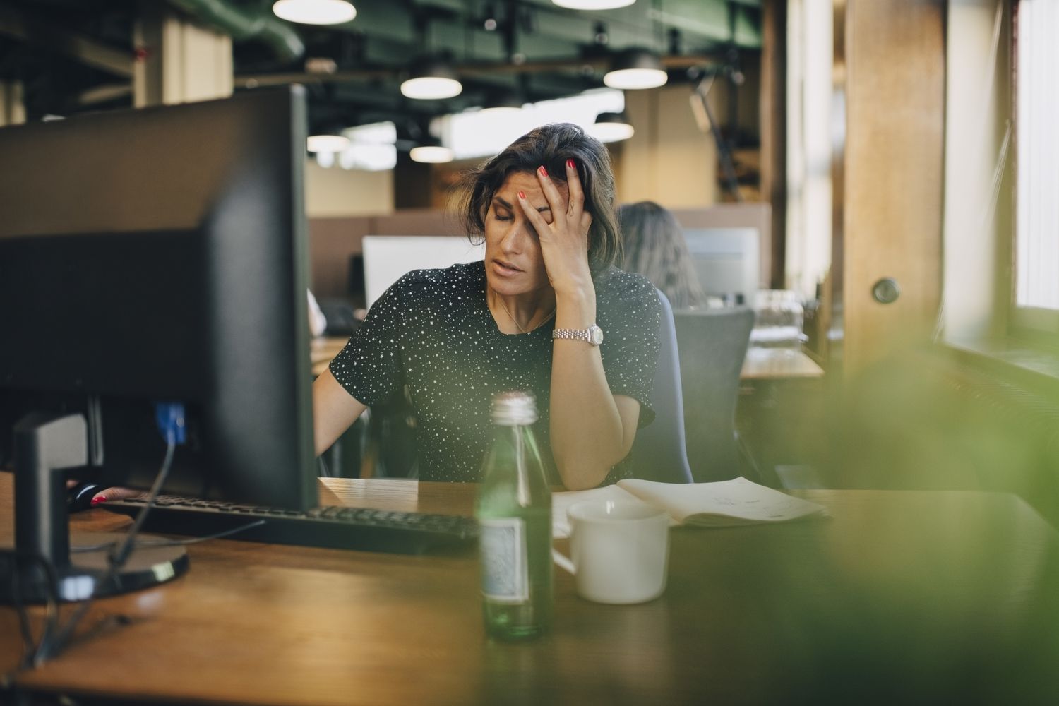 Upset woman with her hand on her head at her office desk