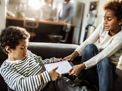 Young Black siblings fighting over digital tablet in the living room.