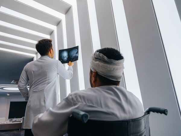 Healthcare professional young doctor examining and analyzing x-ray CT Scan test of human head results of the patients skull with his patient in a medical hospital clinic