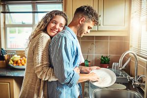 young woman embracing her boyfriend from behind while he does the dishes