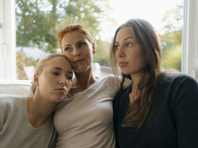 Mother with two teenage girls relaxing on couch at home