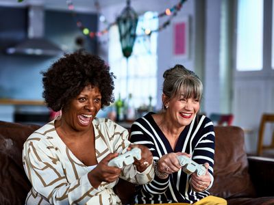 Two middle-aged women smile while holding video game controllers.