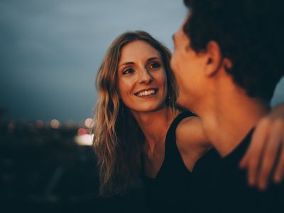 Smiling woman with arm around looking at man while sitting on terrace at dusk 