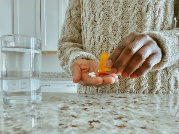 Unrecognizable Woman Pours Pills into Hand from Prescription Bottle