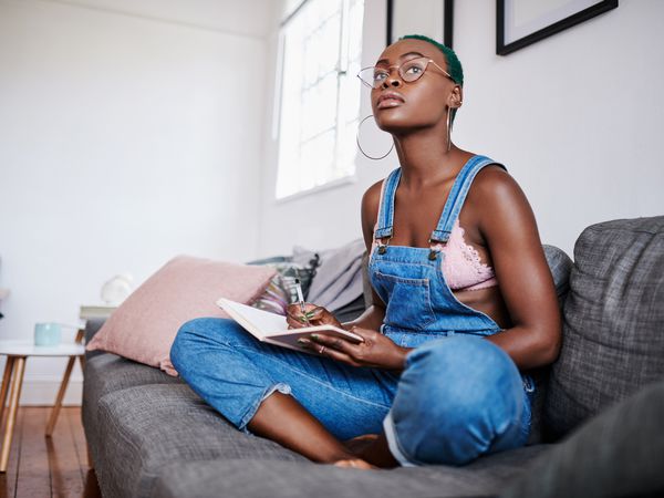 Shot of a young woman writing in a notebook while relaxing on a sofa at home