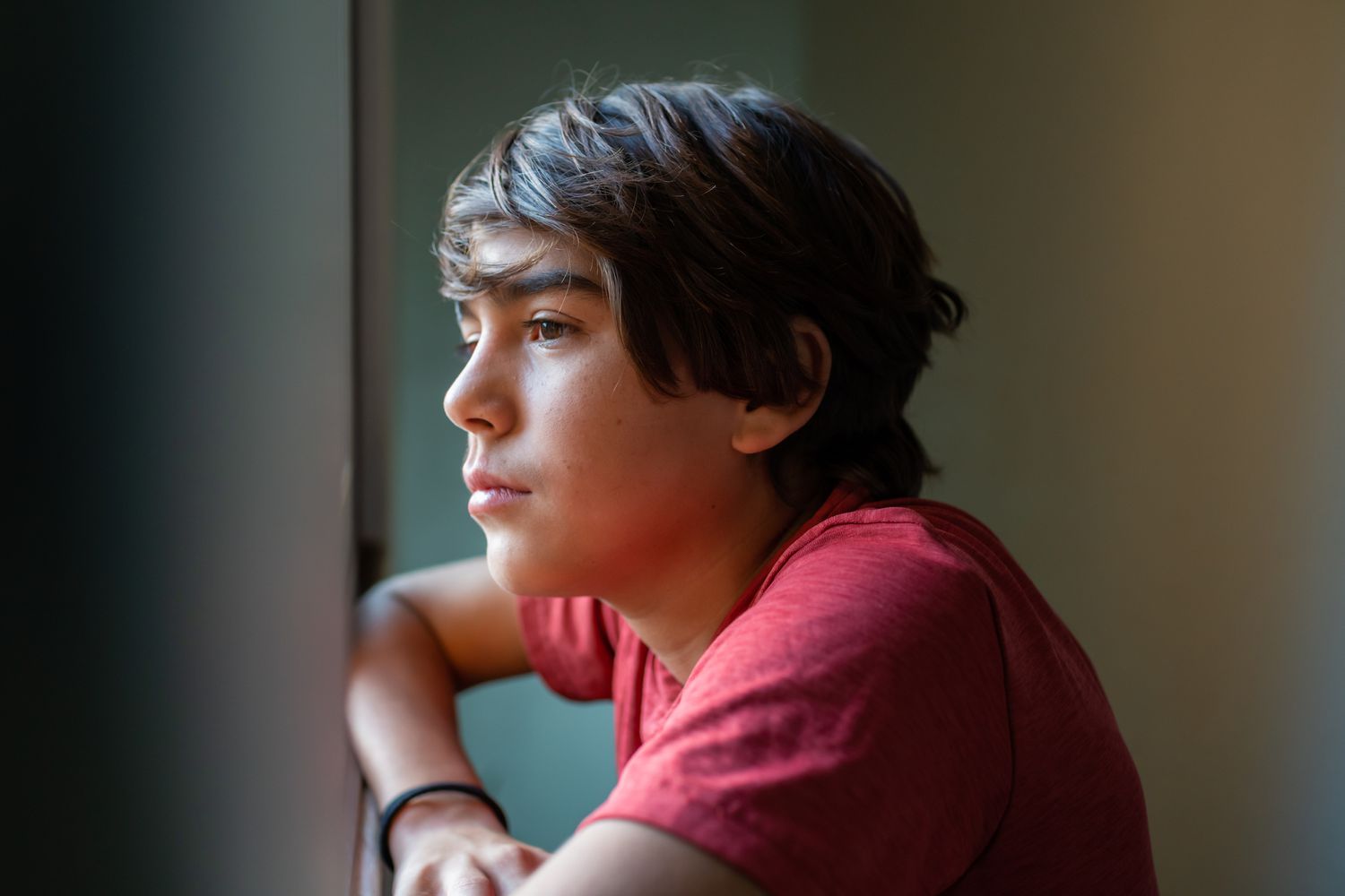 latinx preadolescent boy looking out through window, reflecting, relaxing, pensive