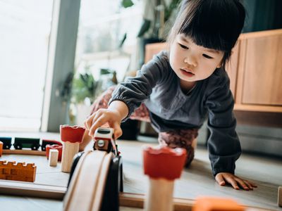 Cute little Asian girl playing with wooden toy train in the living room at home