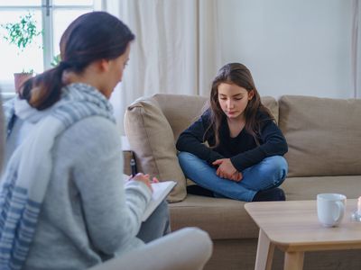 Sad and depressed small girl with therapist sitting indoors, psychotherapy.