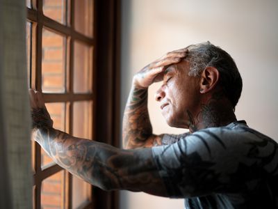 Worried mature man standing at home, close to a window, with hand in the head