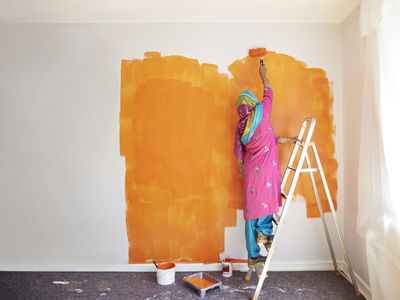 Rear view of senior woman painting wall with orange color while standing on ladder