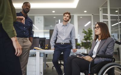 Disabled business woman in wheelchair chatting with coworkers in office