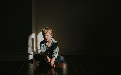 Young boy sits on a dark wooden floor with his legs crossed