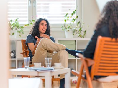 Young Hispanic Male Patient Listening To Female Psychotherapist in her Office