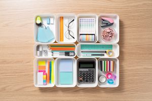 Neatly Organized Stationery in White Trays on Beige Colored Wood Desk Directly Above View.