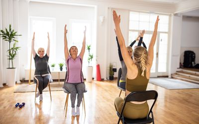 Female yoga instructor having yoga class with senior people on chairs