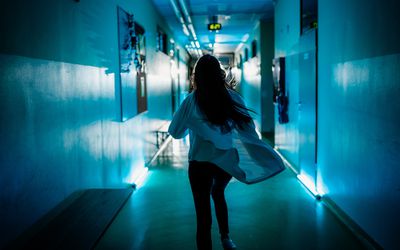 Rear view of female doctor rushing down the corridor of the hospital ward