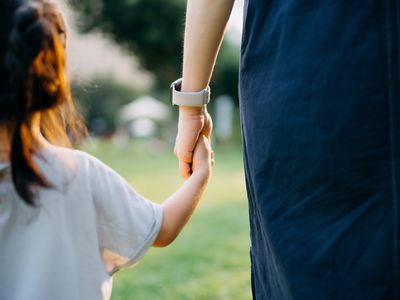 Rear view, close up of young Asian mother walking hand in hand with her little daughter on lawn, relaxing and enjoying family bonding time on a lovely day in park. Family love and care. 