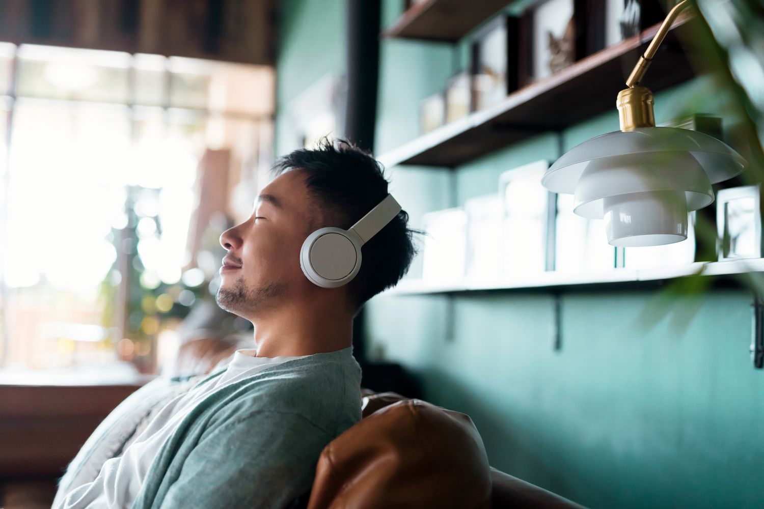 man with eyes closed, enjoying music over headphones while relaxing on the sofa at home