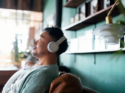 man with eyes closed, enjoying music over headphones while relaxing on the sofa at home