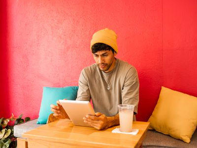 Young Latin student using digital tablet for studying . He is having a soda drink while working