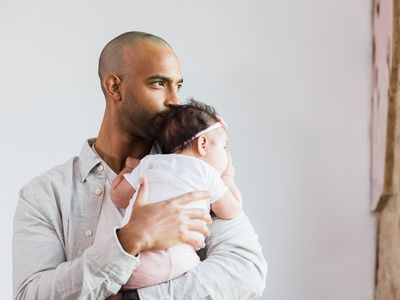 father looks out the window in his home as he carries his baby daughter.