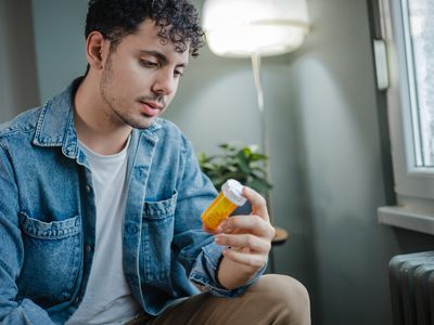 A sad young man in the living room. He suffers from depression and holding bottle of pills