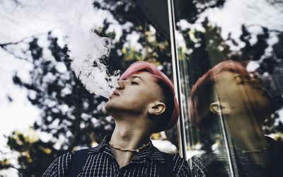 Young hipster with pink colored hair is smoking vape