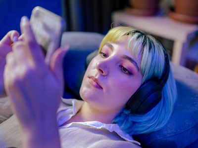 Teenage girl wearing headphones laying down on couch staring at phone in hand