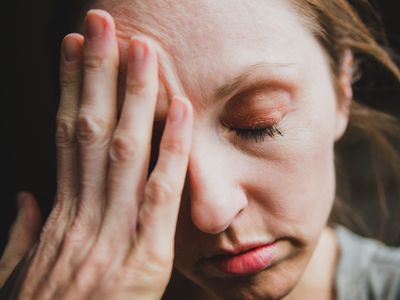 Woman with headache, overwhelmed with stress and anxiety. Mental health conceptual image for depression, injury, or migraine illness. Sad woman looking down and holding hand over eye and forehead. Fatigued woman looks tired and stressed, distraught and exhausted.