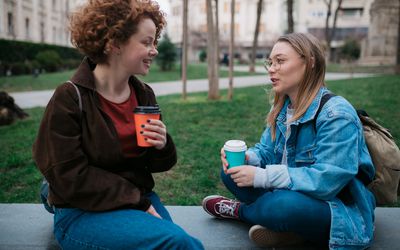 Side view of two happy female friends meeting in a city for a cup of coffee