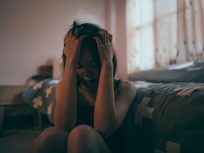 Woman holding head with hands in bedroom, sad