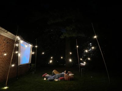 Group of friends hanging out on a blanket in the backyard for an outdoor movie night.