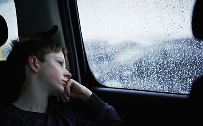 Young boy looking out rainy car window