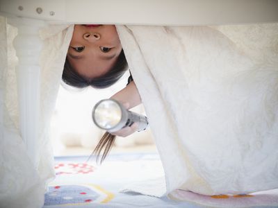 Korean girl looking under bed with flashlight