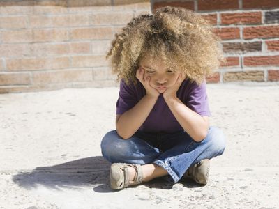 Sad, mixed race boy sitting on sidewalk