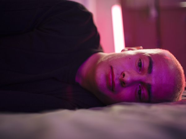 Depressed young man lying on bed in illuminated bedroom at home 