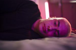 Depressed young man lying on bed in illuminated bedroom at home 