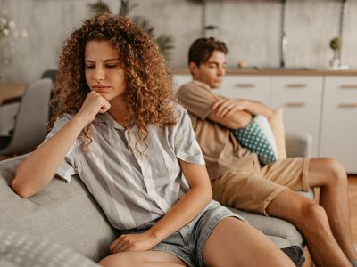 Young couple with relationship problems, sitting on the sofa in the living room and arguing.