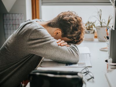 Overwhelmed student resting on their books