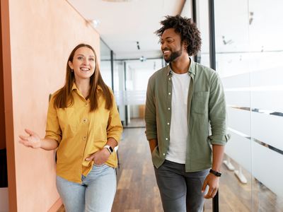 Couple of business people discussing tasks walking in the office hall. Two diverse colleagues have small talk during break. Friendly atmosphere in team