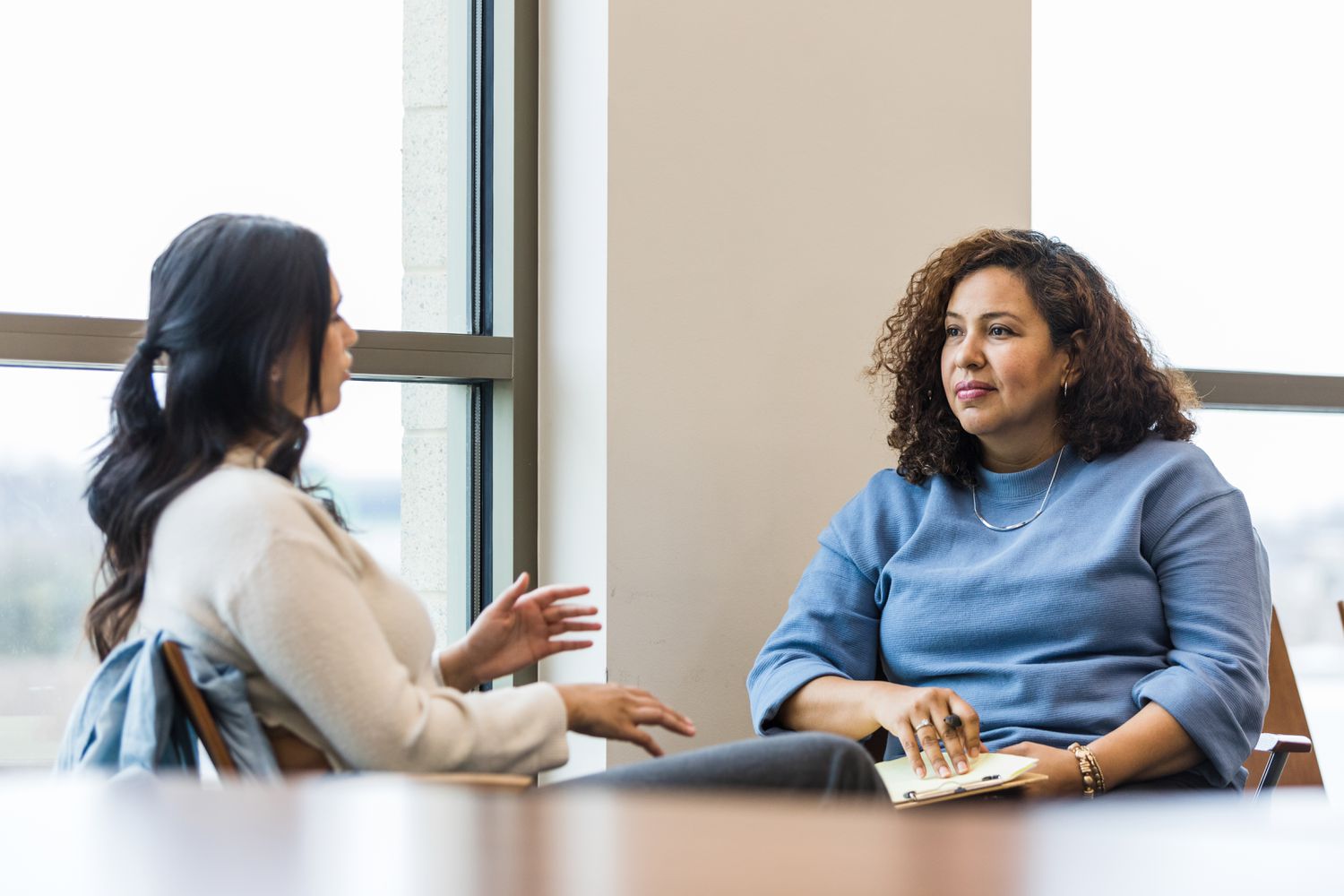 A young adult woman gestures as she shares with her mature adult female counselor.