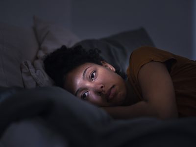 Pensive young woman lying in bed